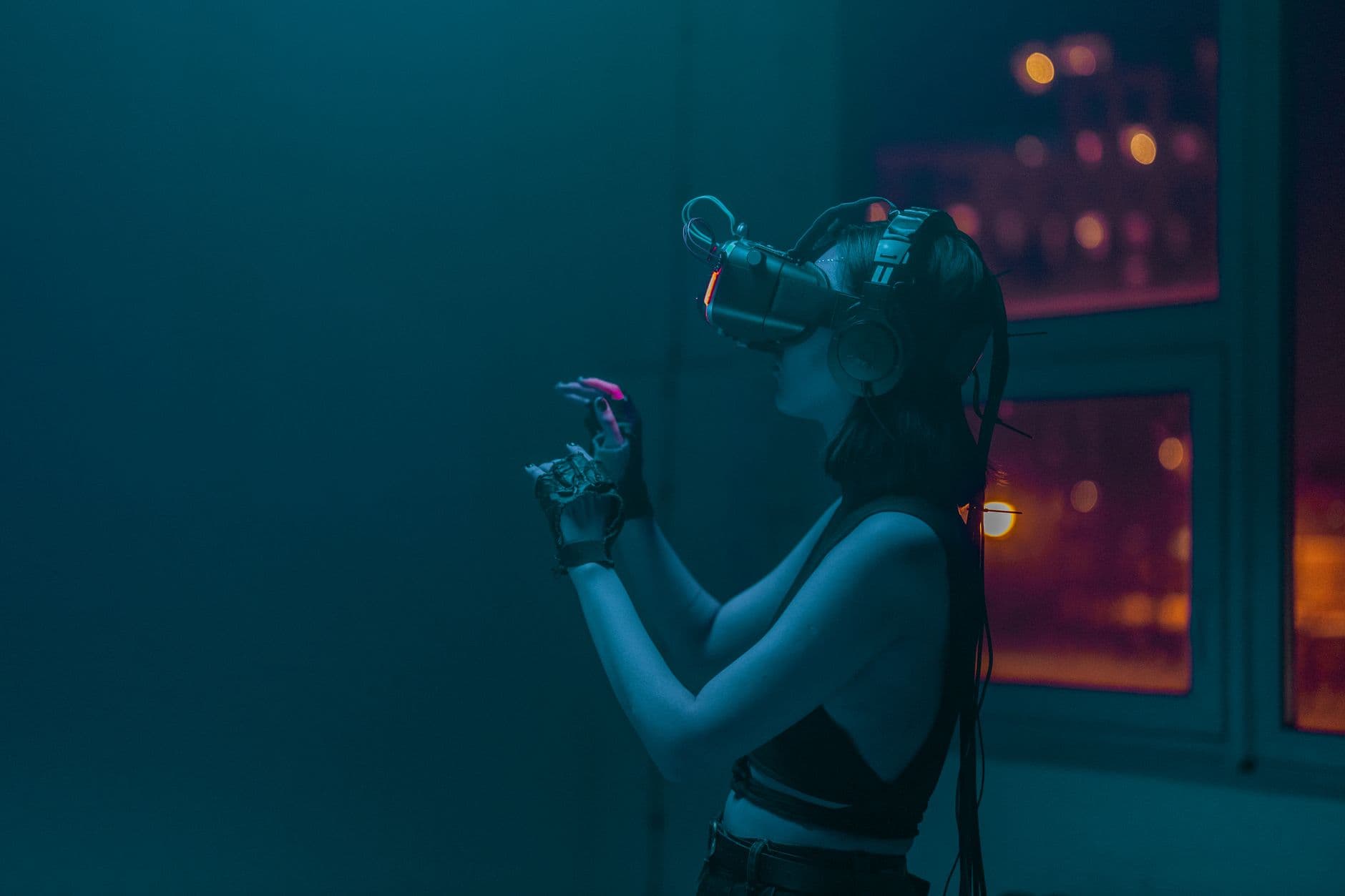 A woman wearing a VR headset and gloves immersed in a virtual reality experience inside a dimly lit room.
